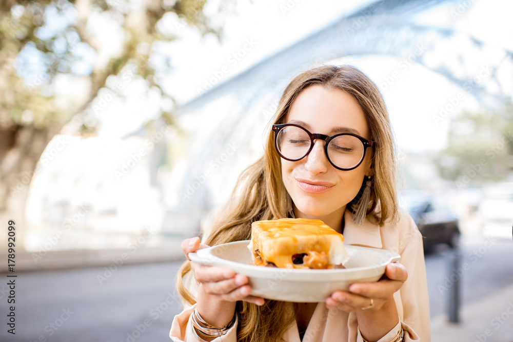 一位年轻女士坐在酒吧里享用传统的葡萄牙肉三明治Francesinha