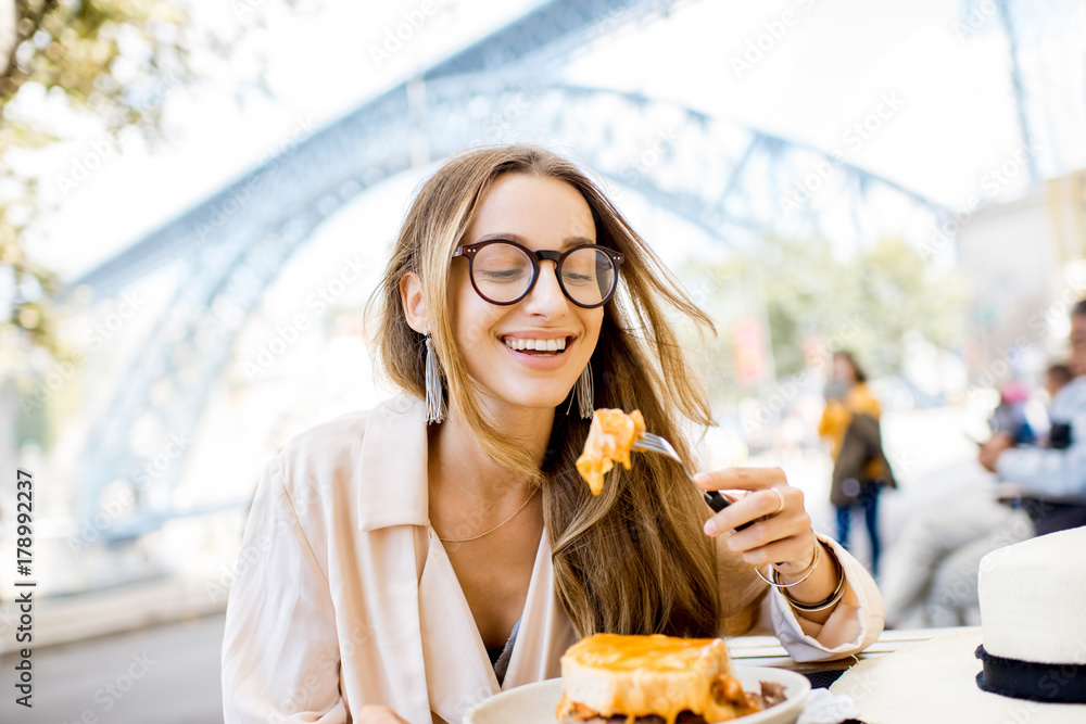 一位女士坐在餐厅里吃着传统的葡萄牙三明治，里面有一种名为francesinha的肉