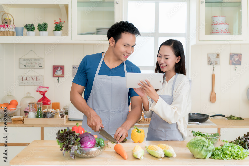 亚洲漂亮的年轻夫妻在家里厨房的数字平板电脑中搜索菜单食谱。H