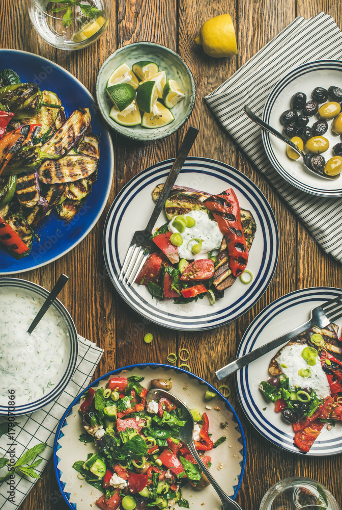 Flat-lay of healthy dinner table setting. Fresh salad, grilled vegetables with yogurt sauce, pickled