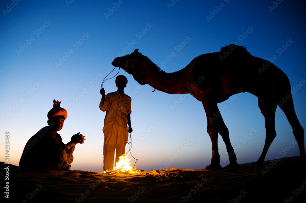 Two indigenous Indian men resting by the bonfire with their camel.