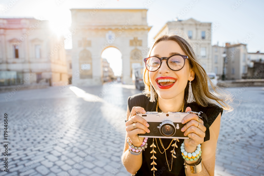 Portrait of a young happy woman tourist with photo camera in front of the famous Triumphal Arch duri