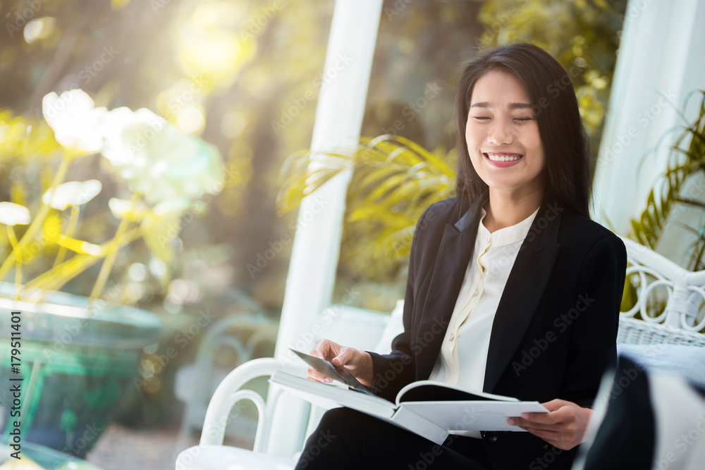 美丽的亚洲女人坐在白色房间内部和花园背景下放松看书