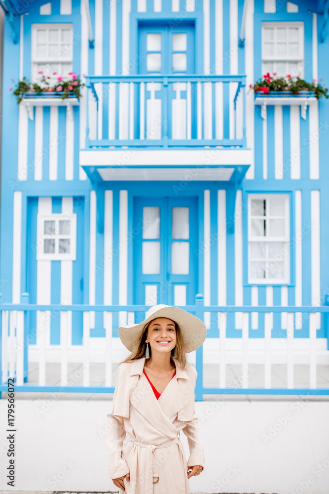 Young woman in sun hat standing with old traditional house facade with blue stripes on the backgroun