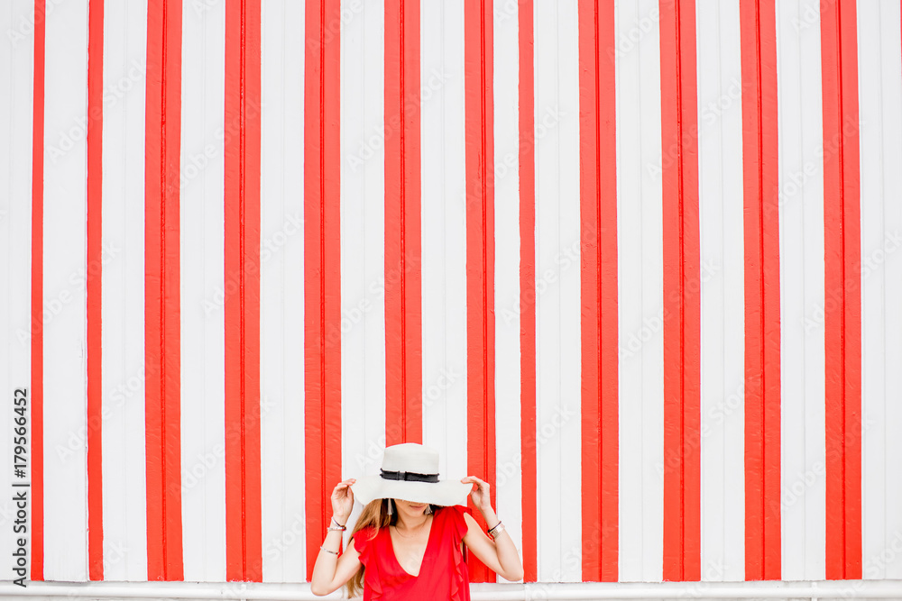 Young woman in red dress on the striped wall background. Wide geometrical view with copy space