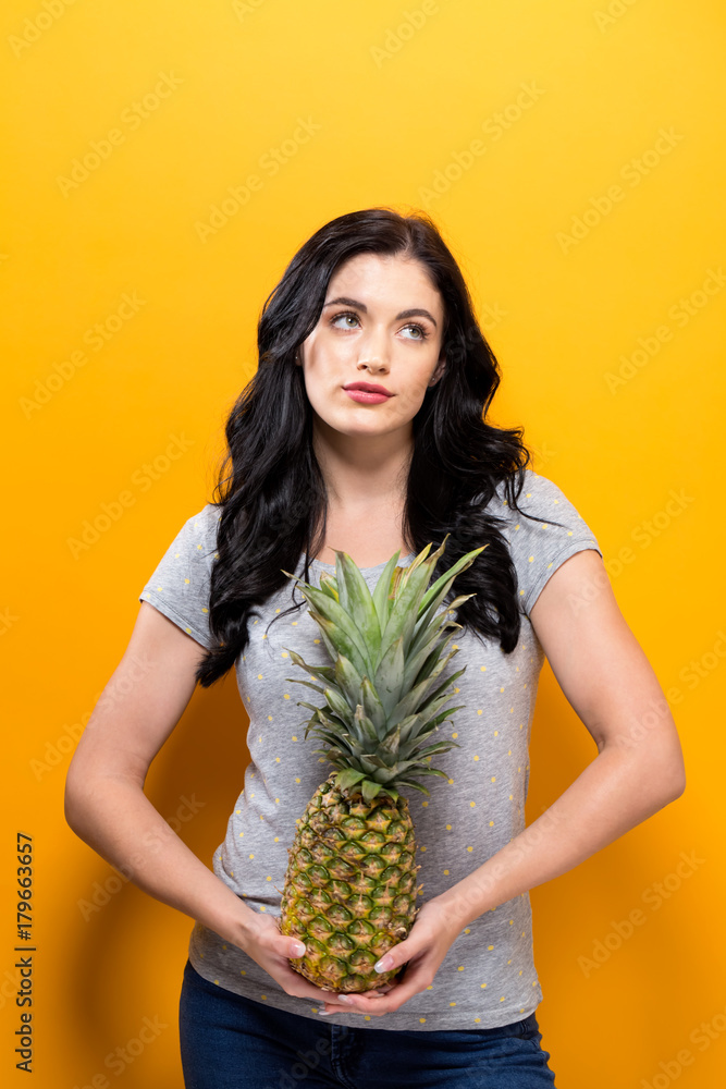 Happy young woman holding a pineapple on a yellow background