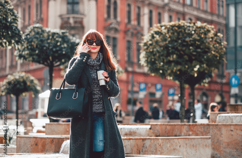 Woman with coffee cup talking on mobile phone in the city