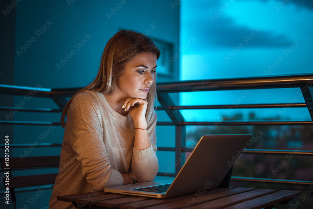 Young beautiful blonde woman working on laptop at night. High ISO image.