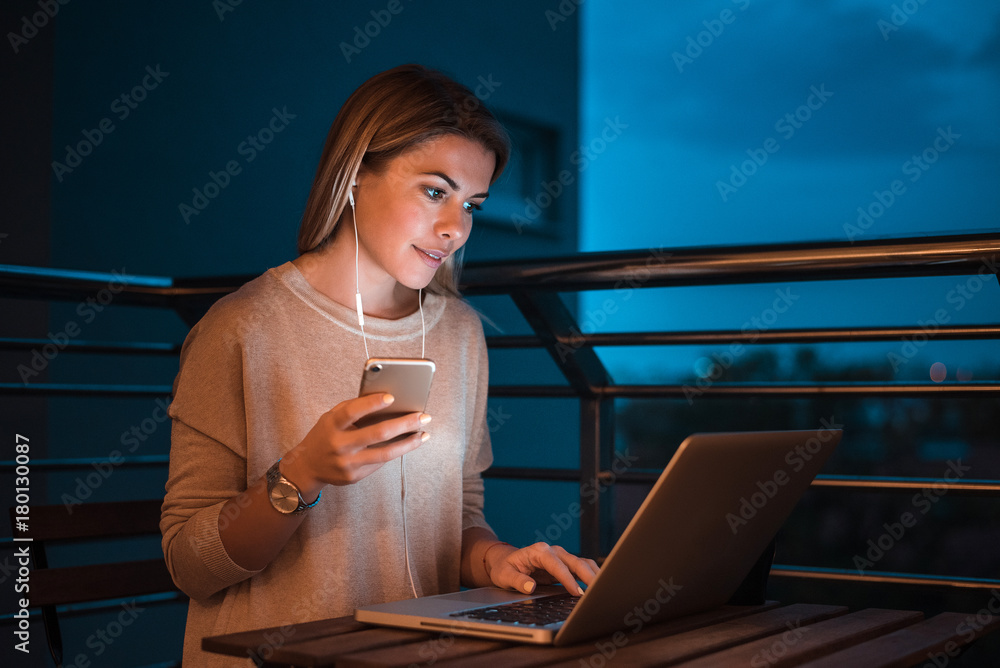 Woman using laptop and phone at night. High ISO image.