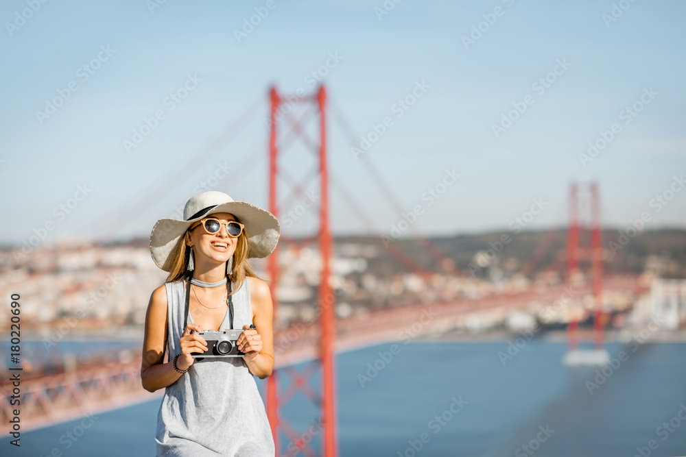 一位年轻女游客的肖像，带着相机坐在风景背景上