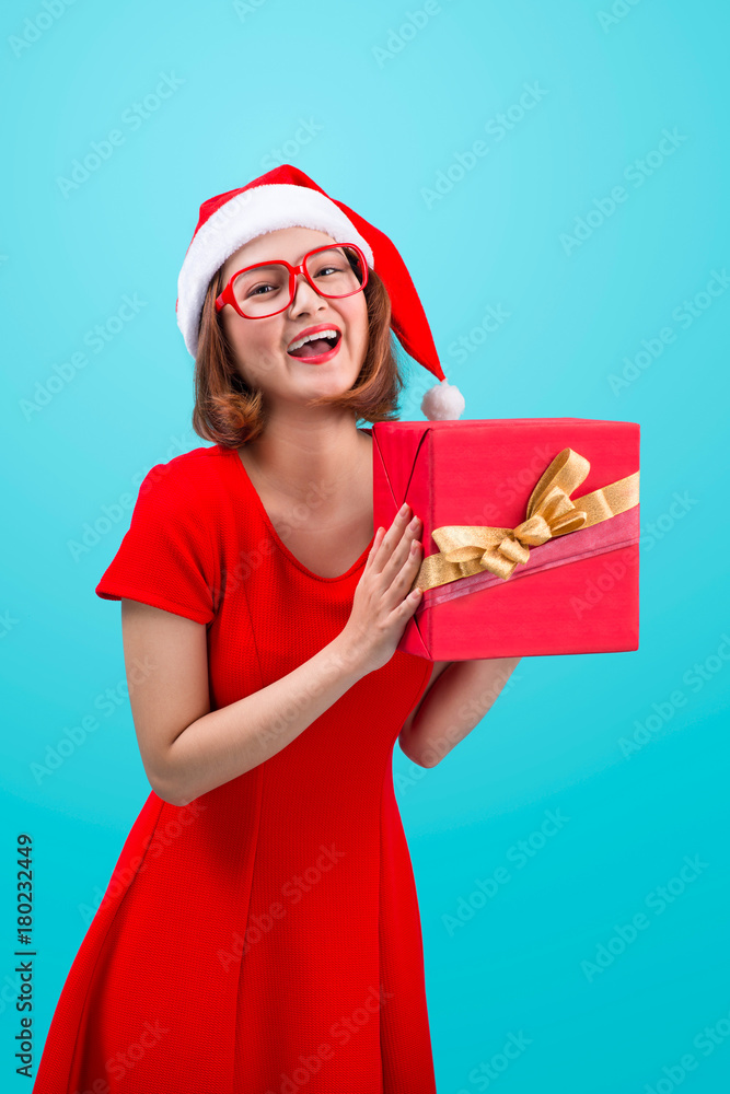 Mrs. Santa. Beautiful young asian woman in santas hat holding a gift isolated on blue.