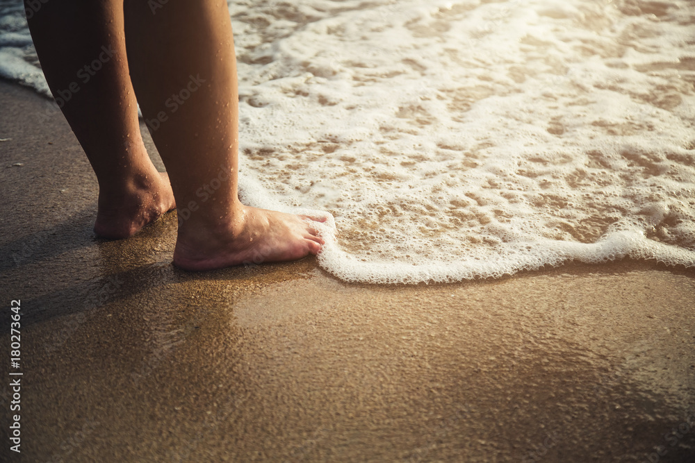 沙滩上美丽的赤脚。海水沙滩泡沫洗涤女性腿部夏季度假co