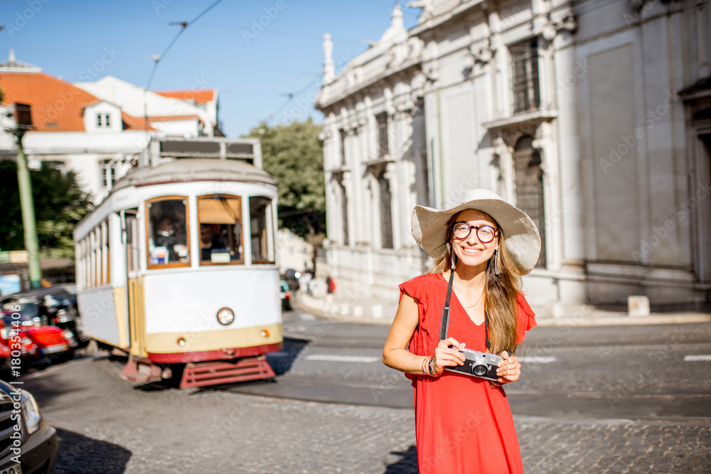 Portrait of a young woman traveler in red dress standing on the street with famous tourist tram on t