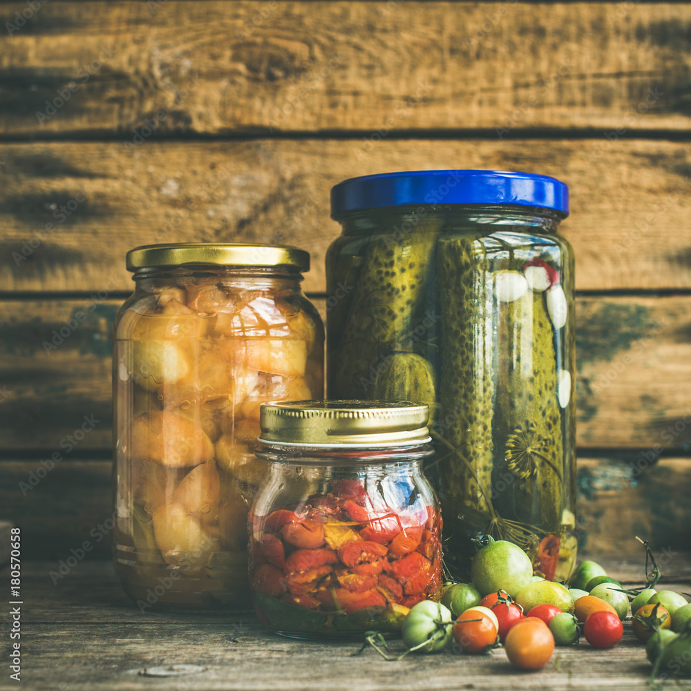 Autumn seasonal pickled vegetables and fruit in glass jars, rustic wooden barn wall background. Fall