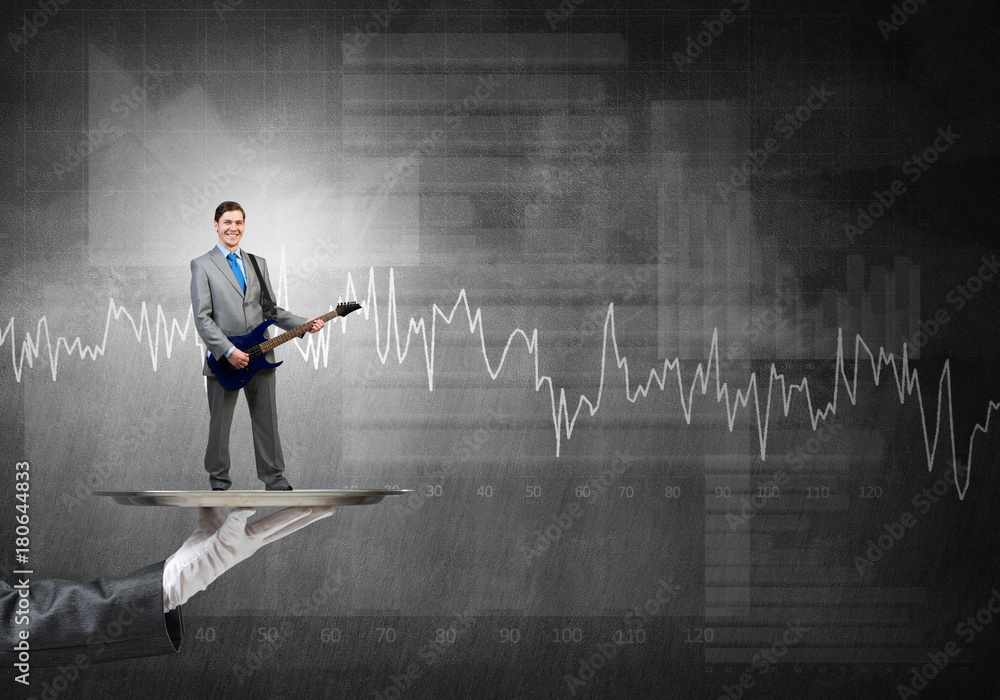 Businessman on metal tray playing electric guitar against graphs background