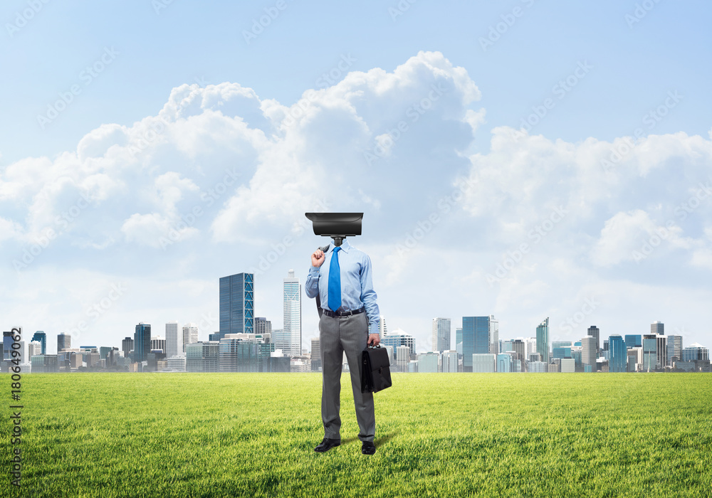 Camera headed man standing on green grass against modern cityscape