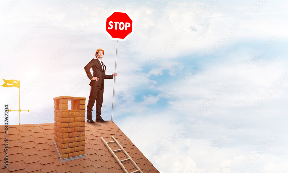 Caucasian businessman on brick house roof showing stop road sign. Mixed media