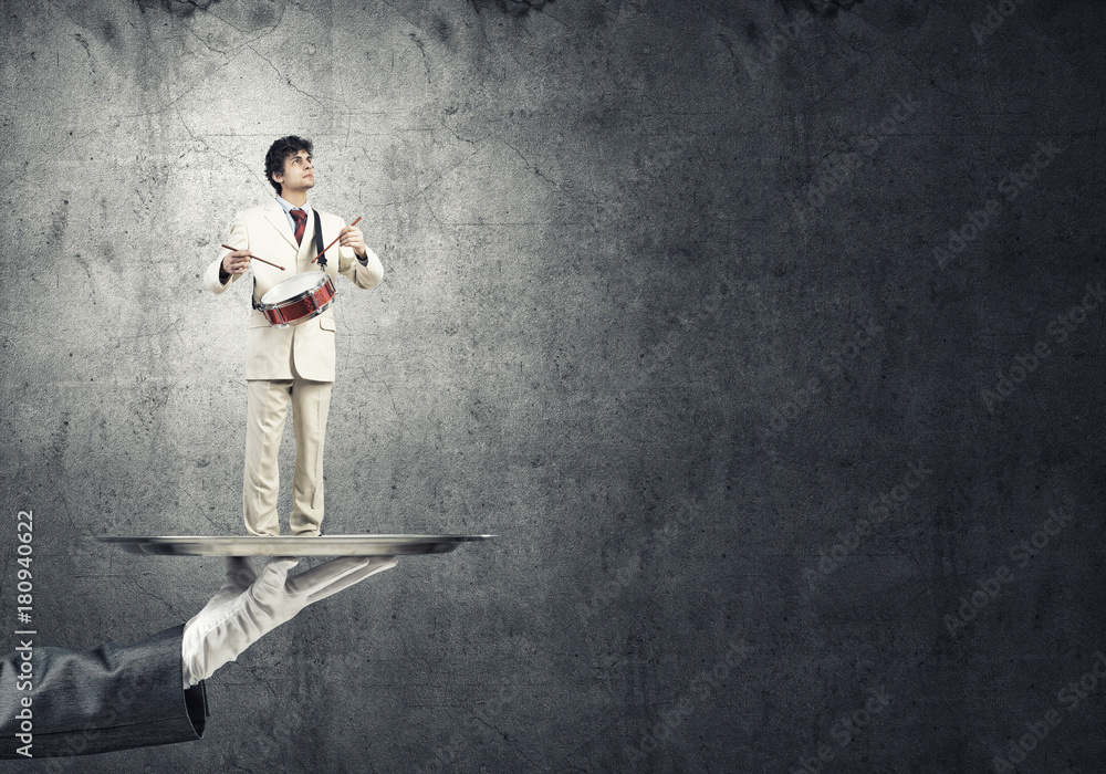 Young businessman on metal tray playing drums against concrete background