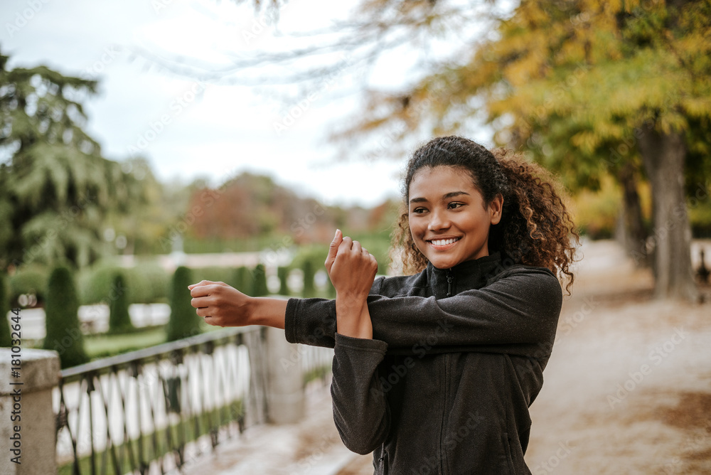 Cheerful young woman doing stretching exercise in park.