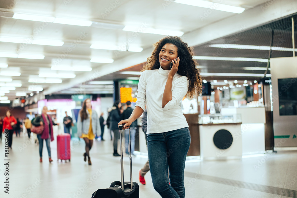 Happy young woman at airport talking on phone.