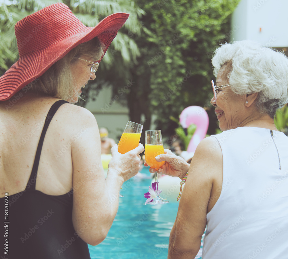 Senior couple women with orange juice by the pool together