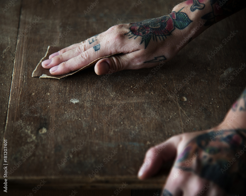 Hands with tattoo using sandpaper on a wood