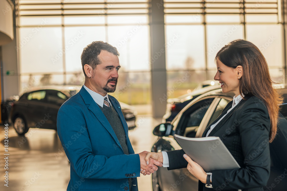 Businesswoman shaking hands with client at car dealership.