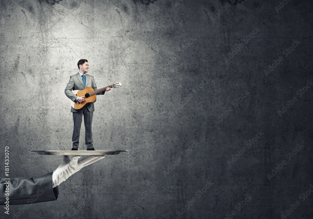 Businessman on metal tray playing acoustic guitar against concrete wall background