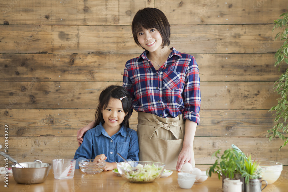 Cute little girl and her beautiful mom.
They are smiling while cooking in kitchen at home.