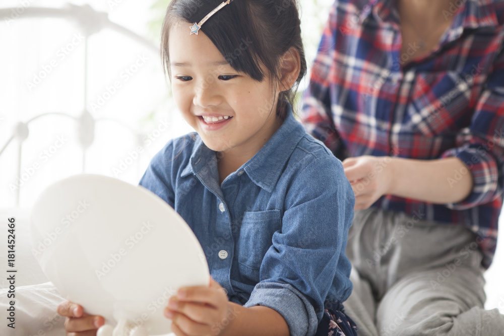 In the bedroom, a young mother is tying her daughters hair.