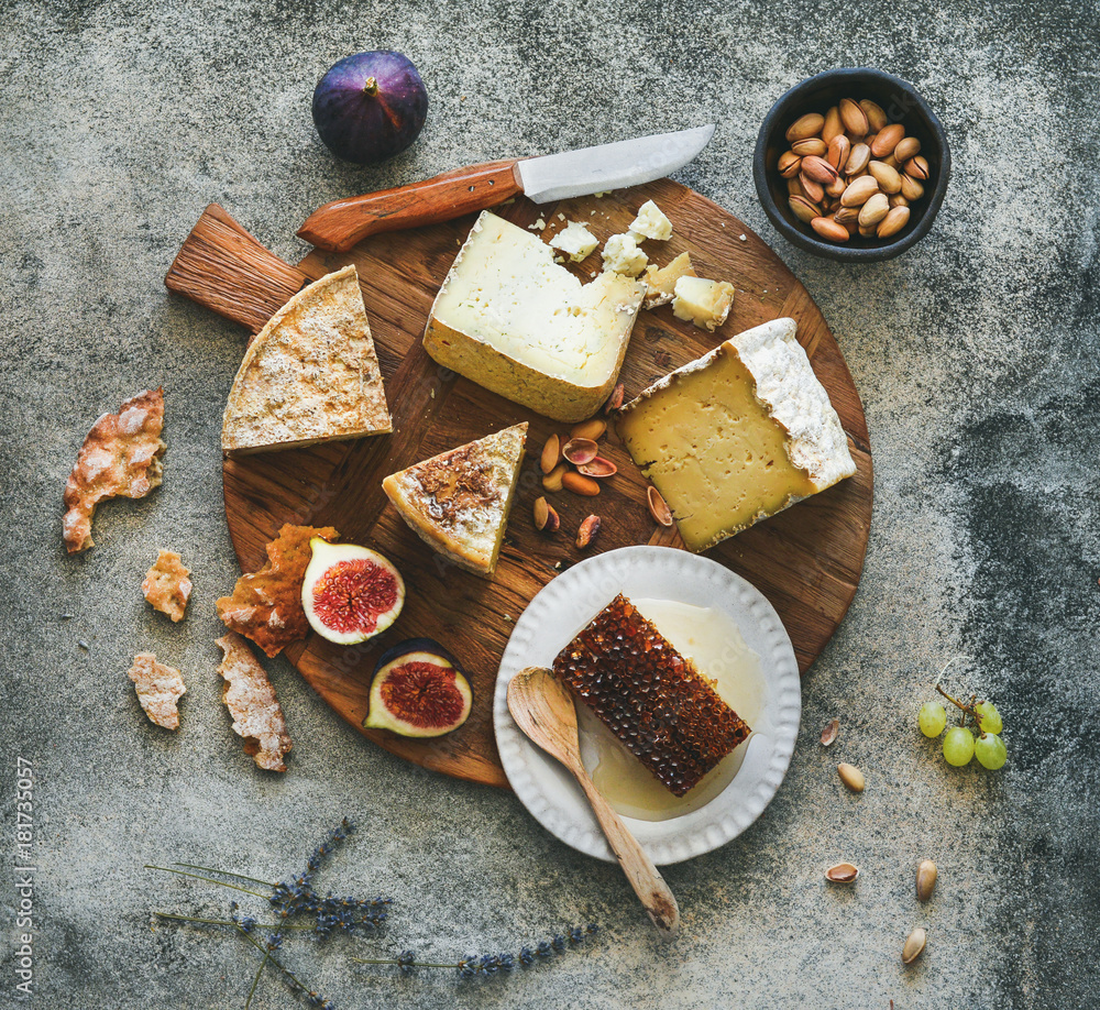 Flat-lay of cheese platter with cheese assortment, figs, honey and nuts over grey concrete backgroun