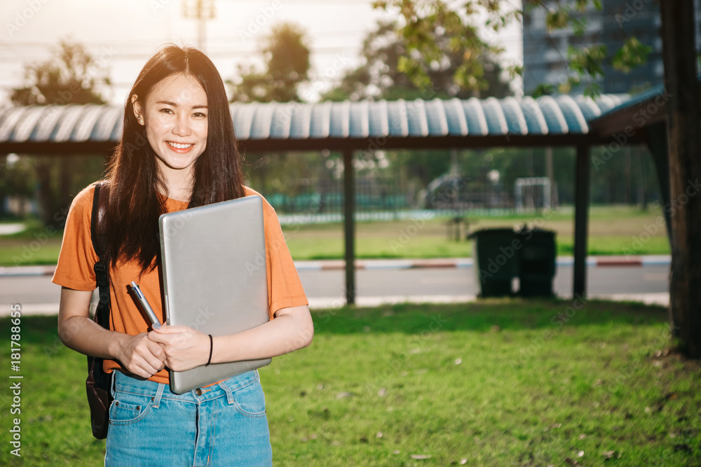 一个年轻或十几岁的亚洲女学生在大学里微笑着看书，看着平板电脑