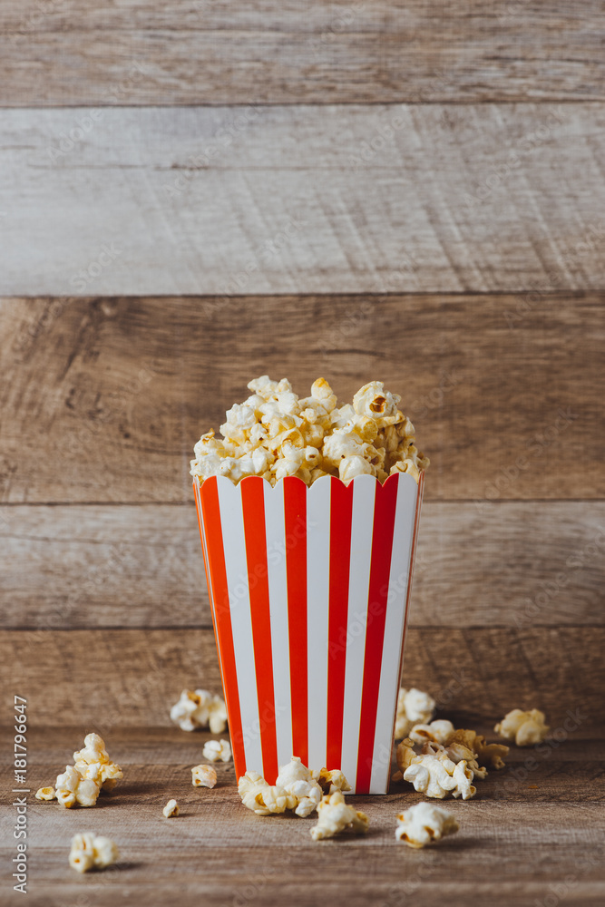 Popcorn in red and white cardboard on wooden table.