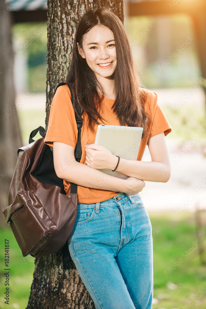 一个年轻或十几岁的亚洲女学生在大学里微笑着看书，看着平板电脑