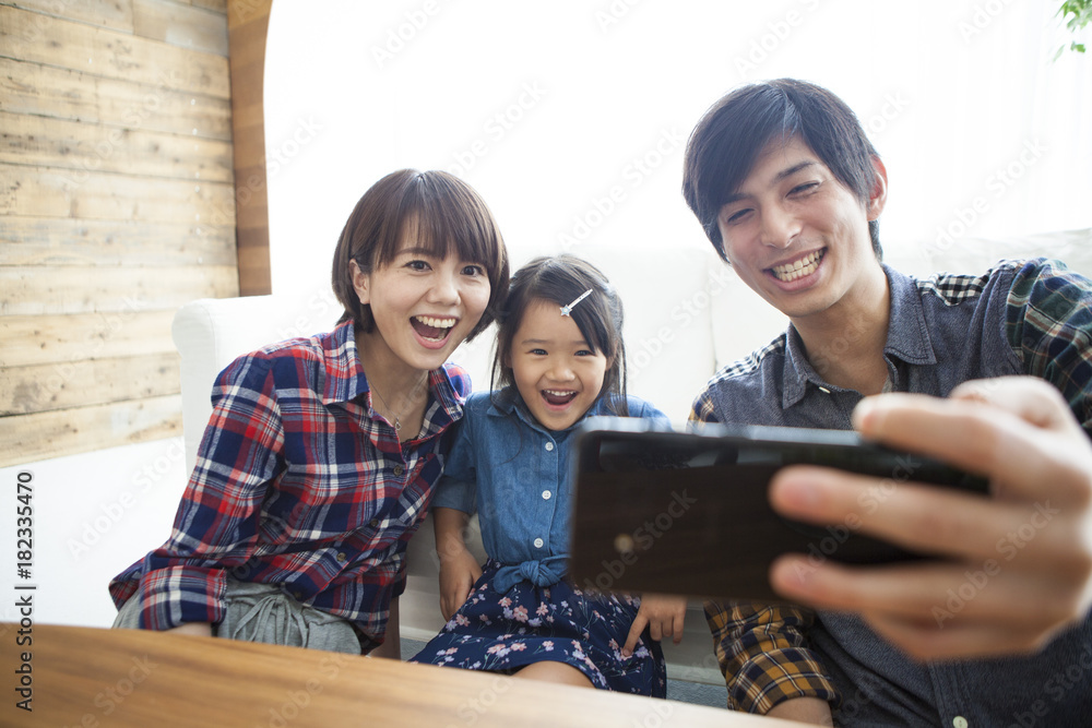 Parents and daughter are sitting on the sofa and using a digital tablet together.