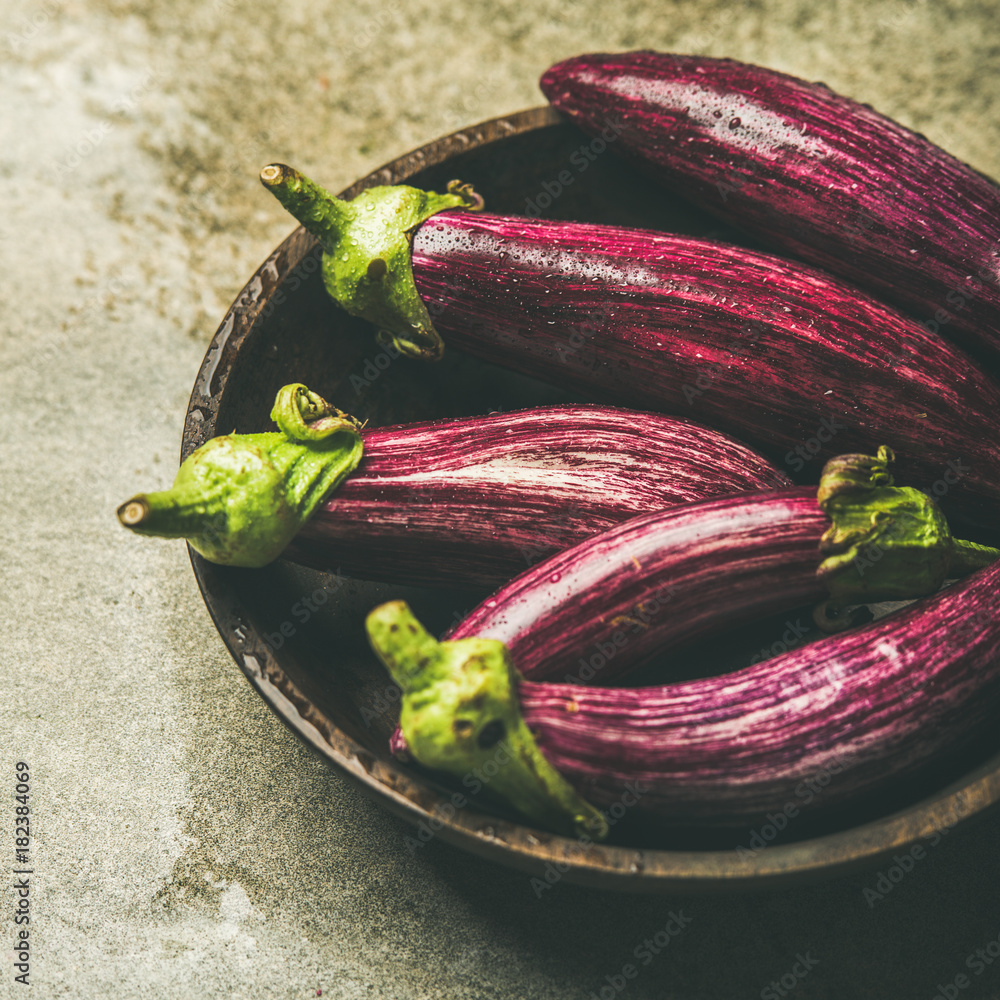 Fresh raw Fall harvest purple eggplants or aubergines in wooden bowl over grey concrete stone backgr