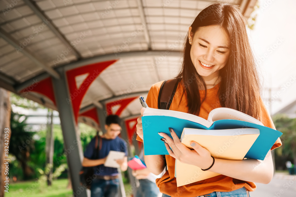 A young or teen asian girl student in university smiling and reading the book and look at the tablet