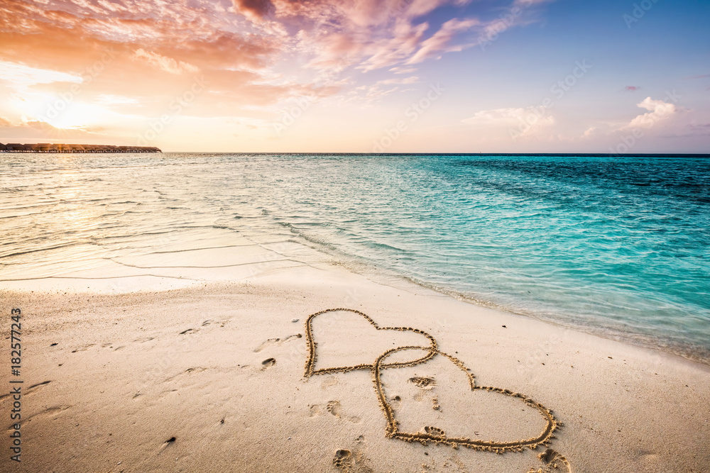 Two hearts drawn on a sandy beach by the sea.