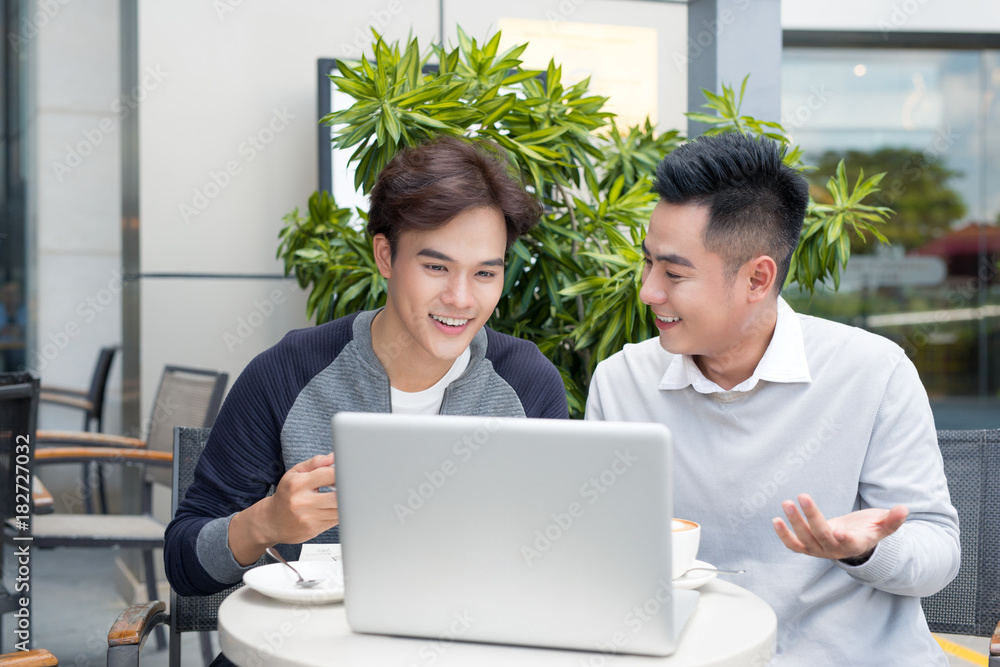 Two businessmen laughing while having a meeting in a classic coffee shop terrace, using a laptop com