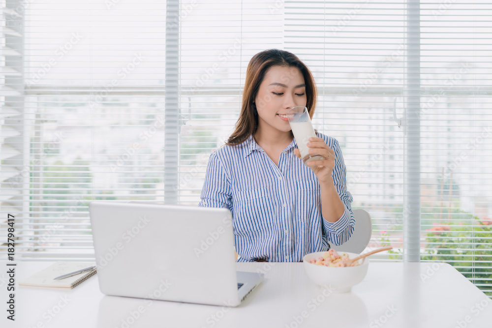 健康的亚洲女性在办公室的办公桌上喝一杯牛奶