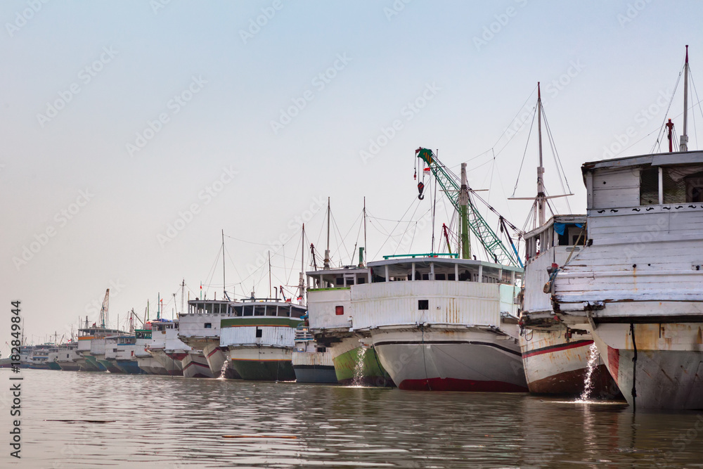 Traditional wooden sailing ships Bugis Pinisi line up in old port of Jakarta - Sunda Kelapa. View fr