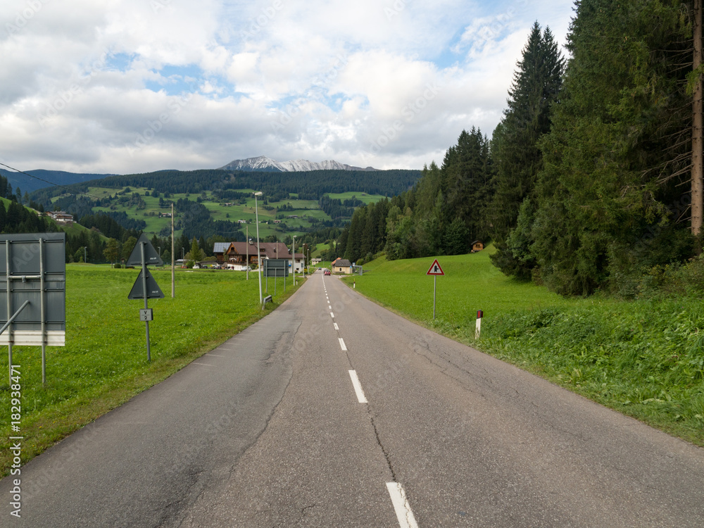 从阿尔卑斯山丘陵和山村背景的低点开始的沥青路。公路旅行co