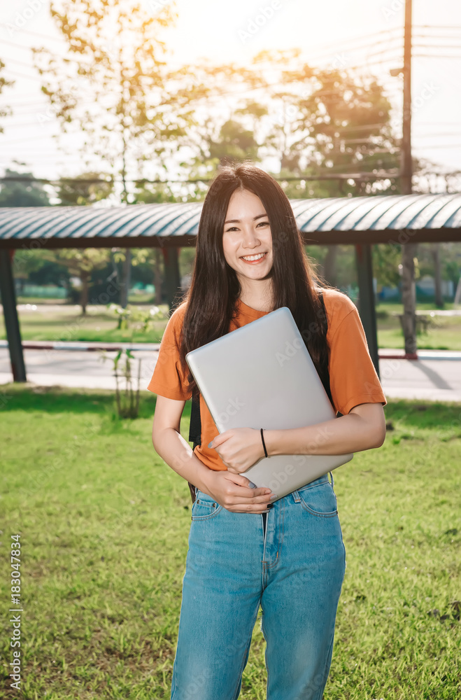 A young or teen asian girl student in university smiling and reading the book and look at the tablet