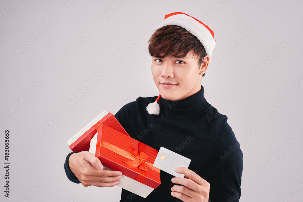 Young attractive asian man in Santa Claus hat holding gift box and credit card