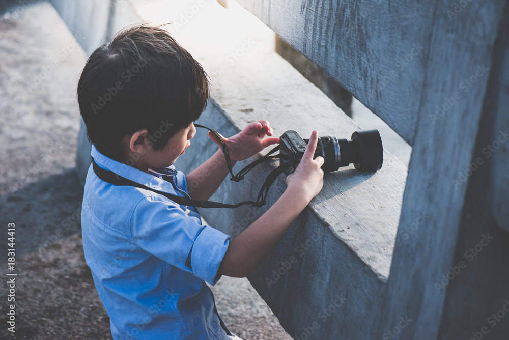 Cute Asian boy taking photo by digital camera outdoors