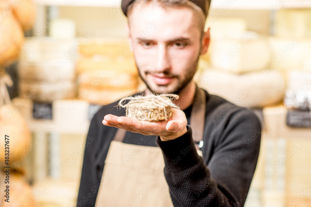 Portrait of a handsome cheese seller in uniform holding young goat cheese in front of the store show