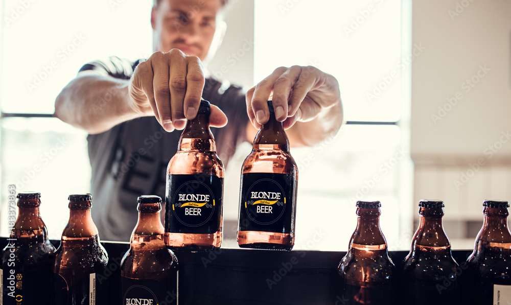 Young man inspecting the beer bottles on conveyor belt