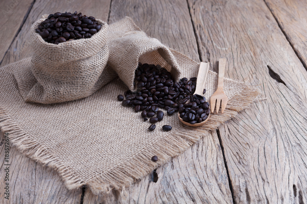 Coffee beans in bag with wooden spoon on old wood plank.