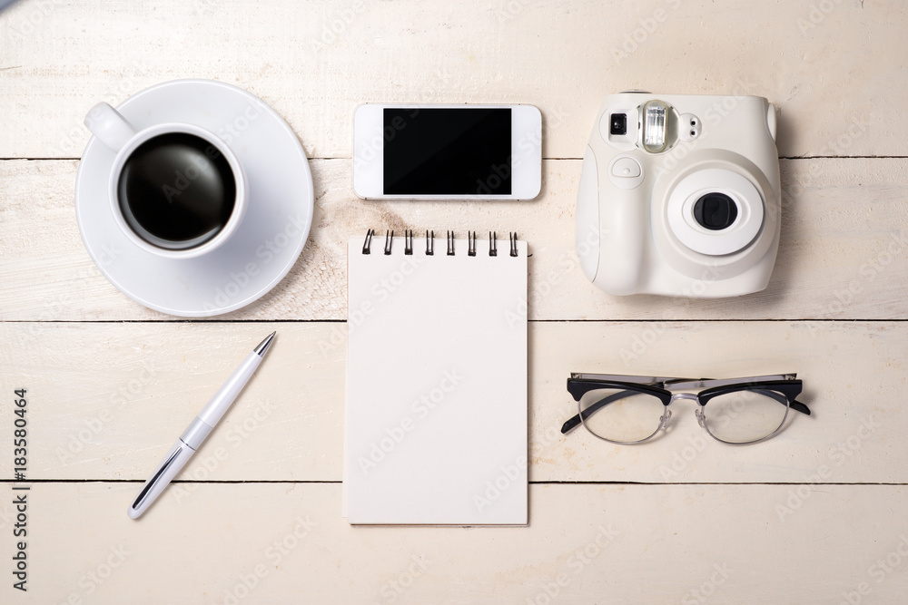 Pen, eyeglasses, coffee, camera, smartphone and notebook on table. Top view.