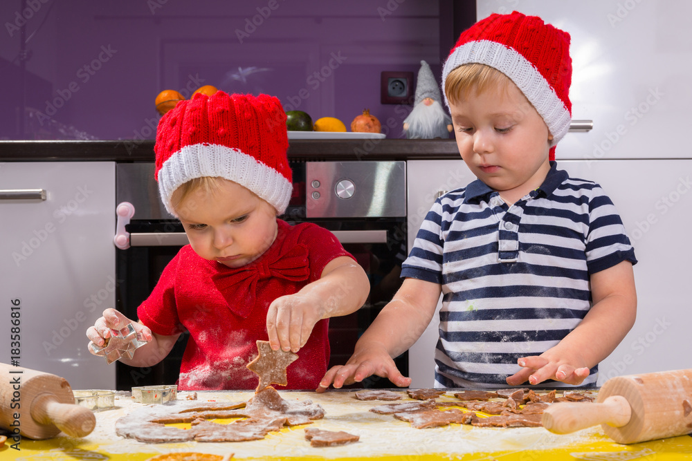 Cute little boy and girl twins preparing Christmas cookies in the kitchen